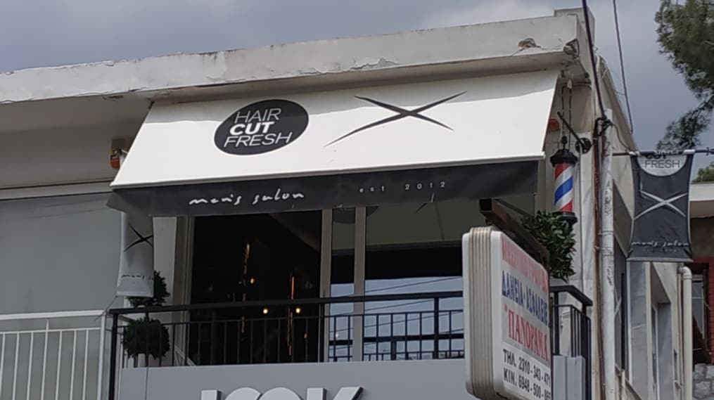 Η τέντα του Haircut Fresh στον πρώτο όροφο: ο κύκλος με το λογότυπο, το X και «men's salon est 2012»